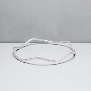 May include: A silver bangle bracelet with a wavy, organic design.
