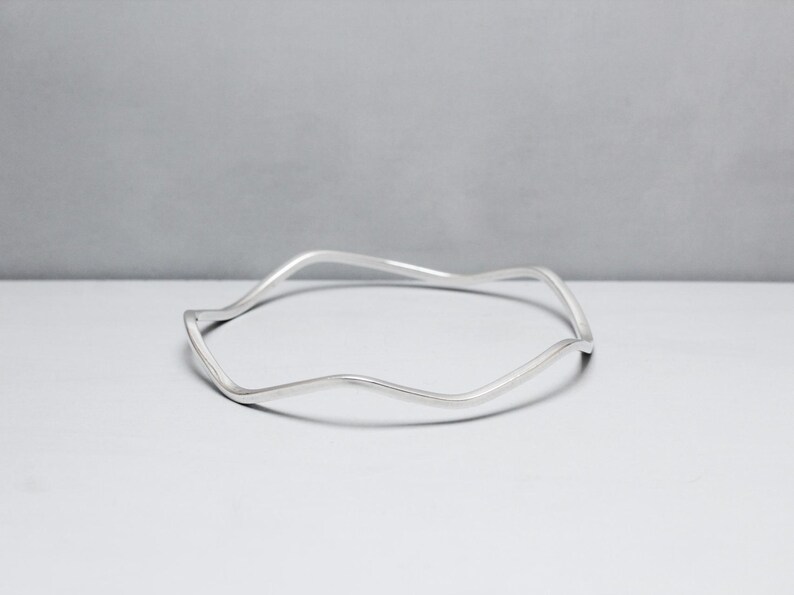 May include: A silver bangle bracelet with a wavy, organic design.
