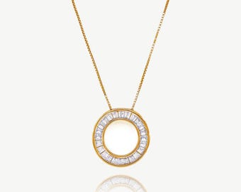 Può includere: Una collana dorata con un pendente circolare. Il pendente è incastonato con pietre preziose rettangolari e trasparenti sul bordo. La catena è sottile e dorata. Il design del pendente crea un effetto alone. Lo sfondo è bianco.