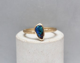 May include: A gold ring with a blue and green opal gemstone set in a textured band.