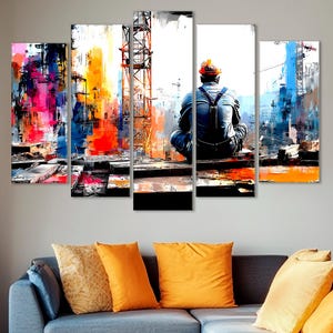 Peut inclure: Impression sur toile en cinq panneaux représentant une scène de construction abstraite. L'œuvre présente un ouvrier du bâtiment assis sur le panneau central, avec des éclaboussures de couleurs vives représentant le paysage urbain et le chantier.