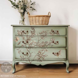 May include: A three-drawer chest of drawers painted in a soft green hue, adorned with a floral branch design. The chest features ornate handles and is topped with a woven basket and a vase of flowers. The text "#670566 branch harmony" is visible.