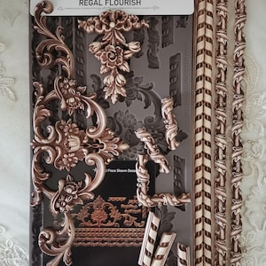May include: A Regal Flourish decor mold set with various ornate designs, including floral and scrollwork elements. The set includes a mold with multiple designs and several pre-made decorative pieces. The mold is 5" x 10" and food safe.
