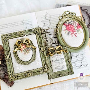 May include: Three ornate, olive green picture frames with gold accents and floral designs. One frame features a bow and poinsettia, another displays a "North Pole Reindeer" print, and the third has a floral arrangement.