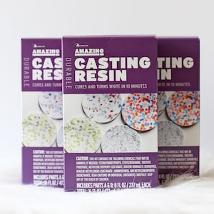 May include: Two purple and white boxes of Alumilite Amazing Durable Casting Resin. The boxes show a close-up of the resin curing in small, colorful, mosaic-like coasters. The text on the boxes reads "Amazing Durable Casting Resin" and "Cures and Turns White in 10 Minutes".