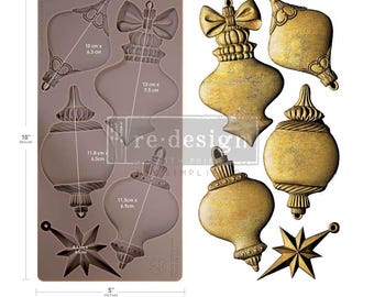 May include: A rectangular brown silicone mold featuring five cavities for casting ornaments, including four bulb shapes and one star. The mold measures 10 inches by 5 inches, with individual cavity dimensions ranging from 8.5 cm to 13 cm in length.