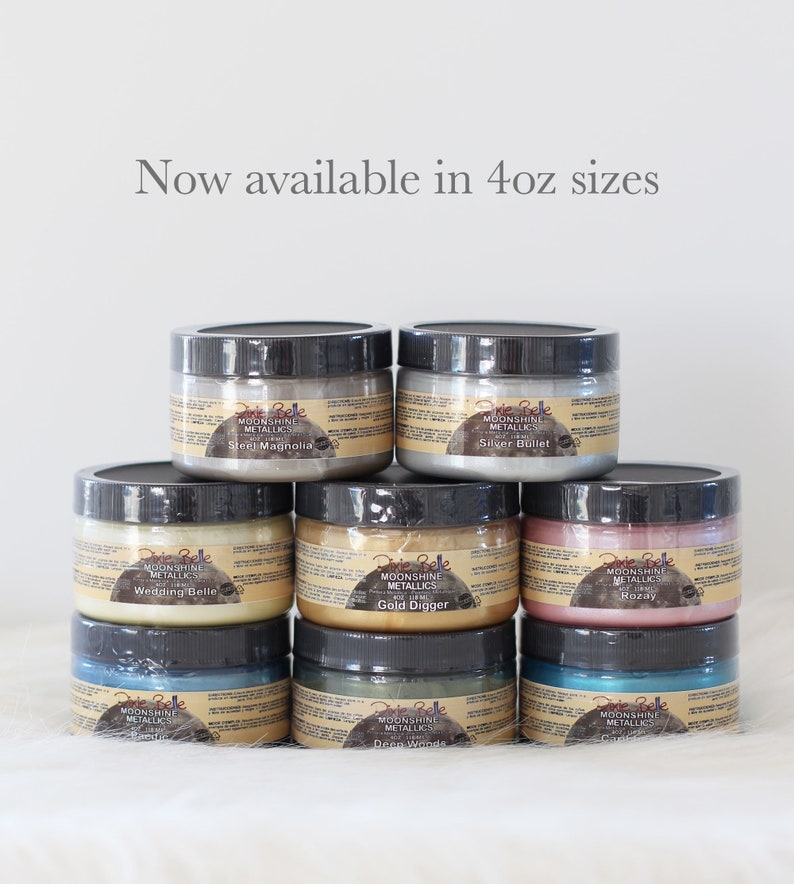 K&ouml;nnte beinhalten: Acht runde Gl&auml;ser mit Dixie Belle Moonshine Metallics Farbe, die in einer Pyramide gestapelt sind. Die Etiketten zeigen den Text Now available in 4oz sizes sowie Farbnamen wie Steel Magnolia, Silver Bullet, Wedding Belle, Gold Digger und Rozay.