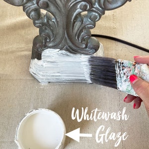 May include: A gray decorative object is being painted with white whitewash glaze. A paintbrush is applying the paint to the object. A container of white glaze is in the foreground. The text "Whitewash Glaze" is in the image.