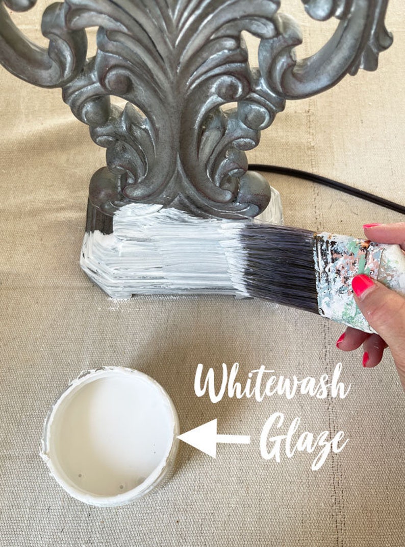 May include: A gray decorative object is being painted with white whitewash glaze. A paintbrush is applying the paint to the object. A container of white glaze is in the foreground. The text "Whitewash Glaze" is in the image.