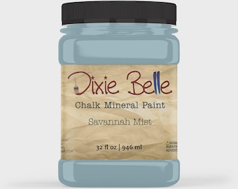 May include: A plastic jar of Dixie Belle Chalk Mineral Paint in the colour Savannah Mist. The label features a tan, textured background with the brand name, product type, and a volume of 32 fl oz | 946 ml. The jar has a black screw-on lid.