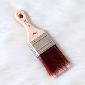 May include: A wooden paint brush with a red and white bristle head. The handle is labeled "Mini" and "Dixie Belle" with the text "Made in USA" on the back.