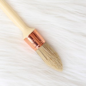 May include: A close-up of a paint brush with a wooden handle and a copper ferrule. The brush has a number "23" printed on the ferrule.