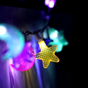 May include: A string of colorful lights with star and moon shapes. The lights are strung on a wire and are lit up, creating a festive atmosphere.