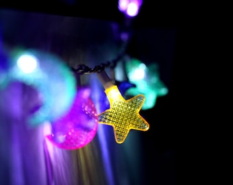May include: A string of colorful lights with star and moon shapes. The lights are strung on a wire and are lit up, creating a festive atmosphere.