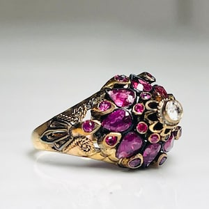 May include: A gold ring with a cluster of pink gemstones and a single white diamond in the center. The ring is set in a floral design.