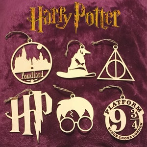 Peut inclure: Six décorations de Noël en bois sur le thème d'Harry Potter. Les décorations sont en forme de Poudlard, du Choixpeau magique, du symbole des Reliques de la Mort, du logo d'Harry Potter, d'Harry Potter avec des lunettes et du quai 9 3/4.