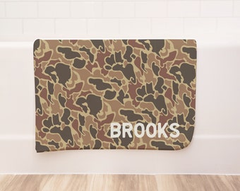 Può includere: Un tappetino da bagno mimetico marrone, beige e rosso con la scritta "BROOKS" stampata in bianco.