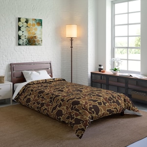 May include: A brown and tan camouflage patterned duvet cover on a twin-sized bed with a white pillow. The bed is in a bedroom with a white brick wall, a floor lamp, and a window.
