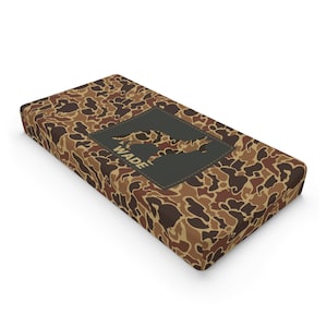 Puede incluir: Una cama para perro de color camuflaje marrón y beige con una silueta negra de un perro y el nombre "WADE" en texto amarillo.