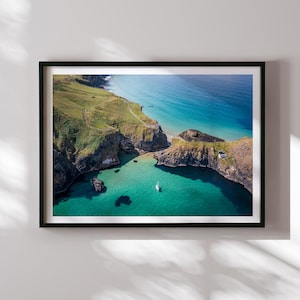 May include: Aerial view of a rocky coastline with a small boat in the turquoise water. The cliffs are covered in green grass and the water is crystal clear.
