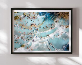 May include: An aerial view of a natural hot spring with many people swimming in the turquoise blue water. The water is surrounded by white rock formations.