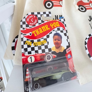May include: A collection of party favors for a child's birthday. The favors include small drawstring bags with a red race car graphic and the text "THANKS FOR RACING". A toy race car is in a plastic package with the text "THANK YOU".