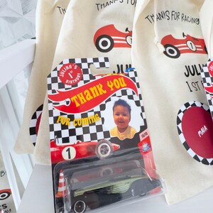 May include: A collection of party favors for a child's birthday. The favors include small drawstring bags with a red race car graphic and the text "THANKS FOR RACING". A toy race car is in a plastic package with the text "THANK YOU".
