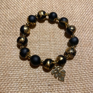 May include: Black and gold beaded bracelet with a gold leaf charm. The beads are matte black with gold flecks.