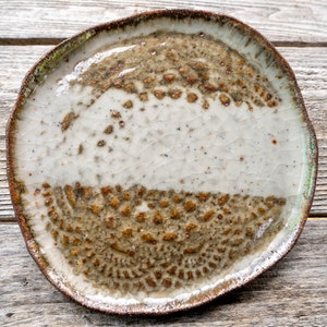 May include: A white ceramic plate with a brown and green glaze. The plate has a crackled finish and a slightly irregular shape.