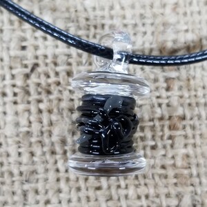 以下が含まれることがあります： ネックレスに付けるための透明なガラスのループが付いた、糸巻き型の黒いガラスのペンダント