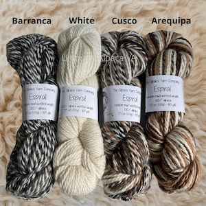 May include: Four skeins of alpaca yarn in different colors: black and white, white, brown and white, and brown and beige. Each skein has a label that reads "The Alpaca Yarn Company Espiral random marl worsted weight 100% alpaca 3.5 oz (100g) - 165 yds".