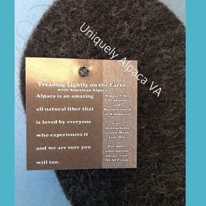 May include: A brown, fuzzy, round piece of alpaca fiber with a tag that reads "Uniquely Alpaca VA" and "Treading Lightly on the Earth with American Alpaca". The tag also includes information about alpaca fiber, care instructions, and a website address.