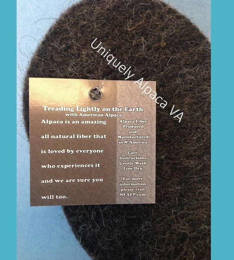 May include: A brown, fuzzy, round piece of alpaca fiber with a tag that reads "Uniquely Alpaca VA" and "Treading Lightly on the Earth with American Alpaca". The tag also includes information about alpaca fiber, care instructions, and a website address.