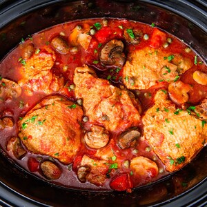 May include: A close-up of a slow cooker filled with chicken, mushrooms, peppers, and a red sauce. The chicken is cooked and the sauce is bubbling.