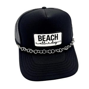 May include: Black trucker hat with a mesh back and a curved brim. The front features a white rectangular patch with the words "BEACH all day" in black script. A silver chain is attached to the brim.