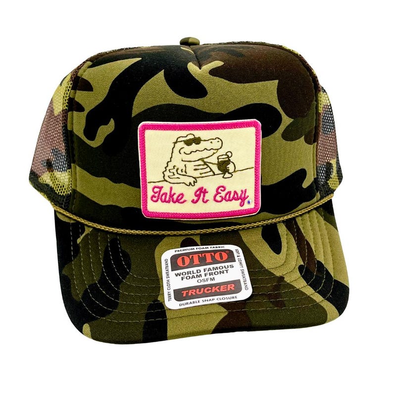 Pode incluir: Bon&eacute; de caminhoneiro camuflado com costas em malha e um patch com um jacar&eacute; com &oacute;culos de sol e uma bebida. O patch diz "Take It Easy" em script rosa. O bon&eacute; tem um fecho de press&atilde;o.