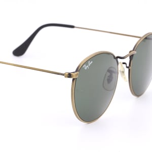 Puede incluir: Gafas de sol redondas doradas con lentes verdes y el logotipo de Ray-Ban en el marco.