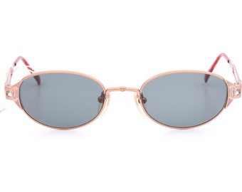 May include: A pair of oval-shaped sunglasses with a rose gold metal frame and dark gray lenses.
