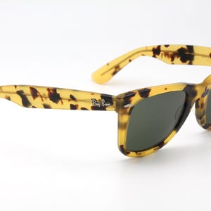 Puede incluir: Gafas de sol Ray-Ban cl&aacute;sicas con un dise&ntilde;o de carey. Las monturas son amarillas y marrones, con lentes verde oscuro. El logotipo de Ray-Ban es visible en la patilla. Un accesorio elegante para la protecci&oacute;n ocular.