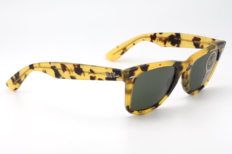 Puede incluir: Gafas de sol Ray-Ban cl&aacute;sicas con un dise&ntilde;o de carey. Las monturas son amarillas y marrones, con lentes verde oscuro. El logotipo de Ray-Ban es visible en la patilla. Un accesorio elegante para la protecci&oacute;n ocular.