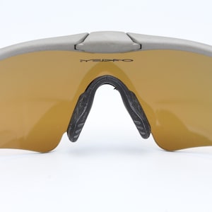 May include: Gray wraparound sunglasses with gold mirrored lenses. The sunglasses have a black nose bridge and black temple tips.