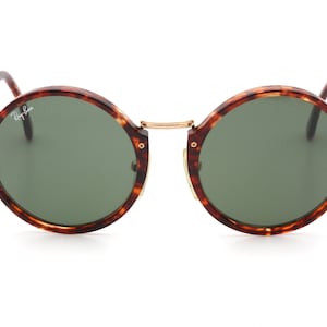 May include: Round tortoiseshell sunglasses with green lenses. The sunglasses have a gold metal bridge and gold accents.
