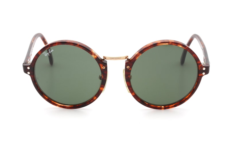 May include: Round tortoiseshell sunglasses with green lenses. The sunglasses have a gold metal bridge and gold accents.