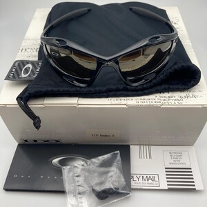 May include: Black sunglasses with a brown lens and a black microfiber pouch. The sunglasses have a UV index of 3. The pouch has the Oakley logo on it.