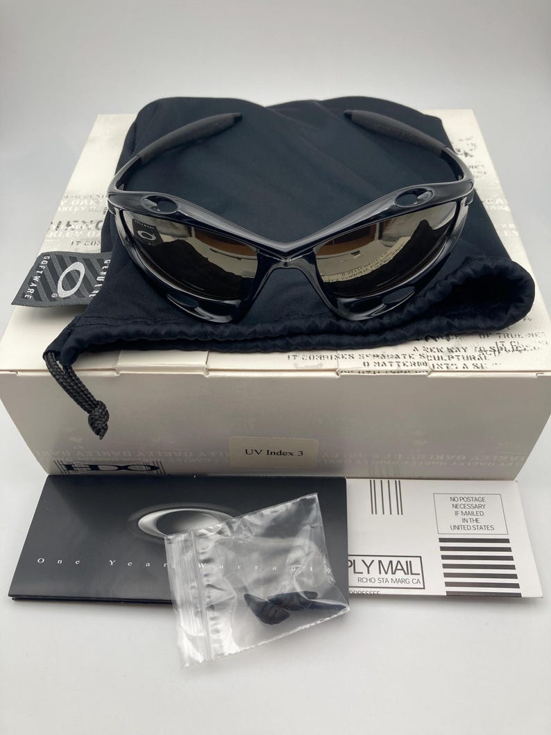 May include: Black sunglasses with a brown lens and a black microfiber pouch. The sunglasses have a UV index of 3. The pouch has the Oakley logo on it.
