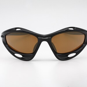 May include: Black sunglasses with brown lenses and a curved, wraparound design.