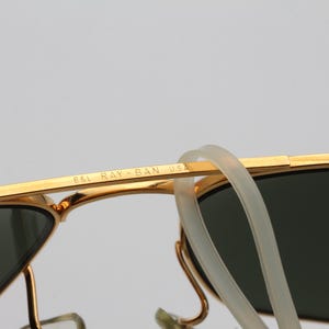 May include: Gold-tone aviator sunglasses with green lenses and a B&L Ray-Ban USA inscription on the frame.