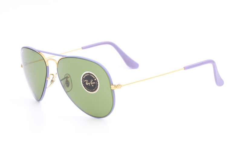 Op de afbeelding: Paarse en gouden aviator zonnebril met groene glazen. De zonnebril heeft een Ray-Ban logo op de rechter lens.