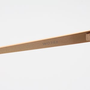 May include: Close-up of the gold-toned metal arm of a pair of sunglasses. The arm is engraved with the model number "W0756".