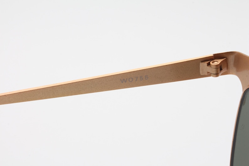 May include: Close-up of the gold-toned metal arm of a pair of sunglasses. The arm is engraved with the model number "W0756".